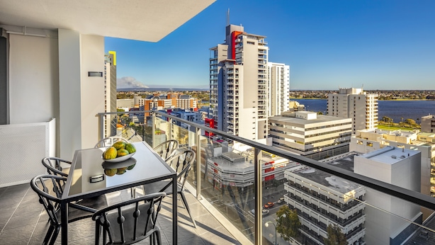 A balcony with a table and chairs, overlooking a cityscape with buildings and a body of water. - Quest East Perth (East Perth)