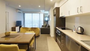 A modern kitchen with a dining area, a sofa, and a television in a living room. - Quest East Perth (East Perth)