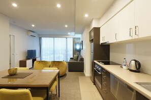 A modern kitchen with a dining area, a sofa, and a television in a living room. - Quest East Perth (East Perth)