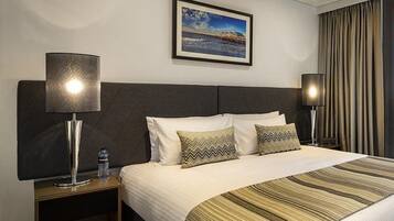 A hotel room with a large bed, two bedside lamps, a water bottle, and a framed picture on the wall.