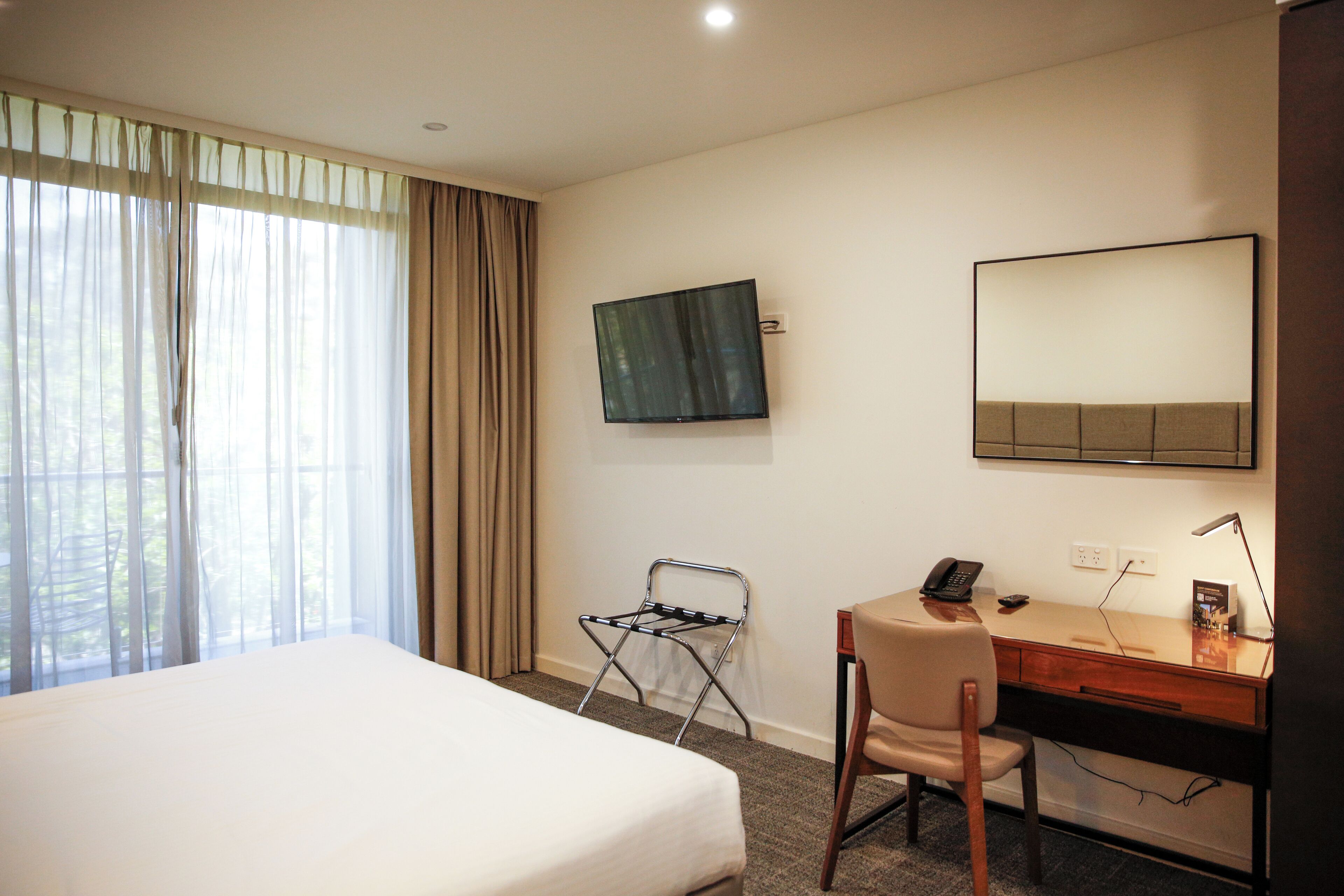 A hotel room with a bed, desk, chair, TV, and a window with curtains.