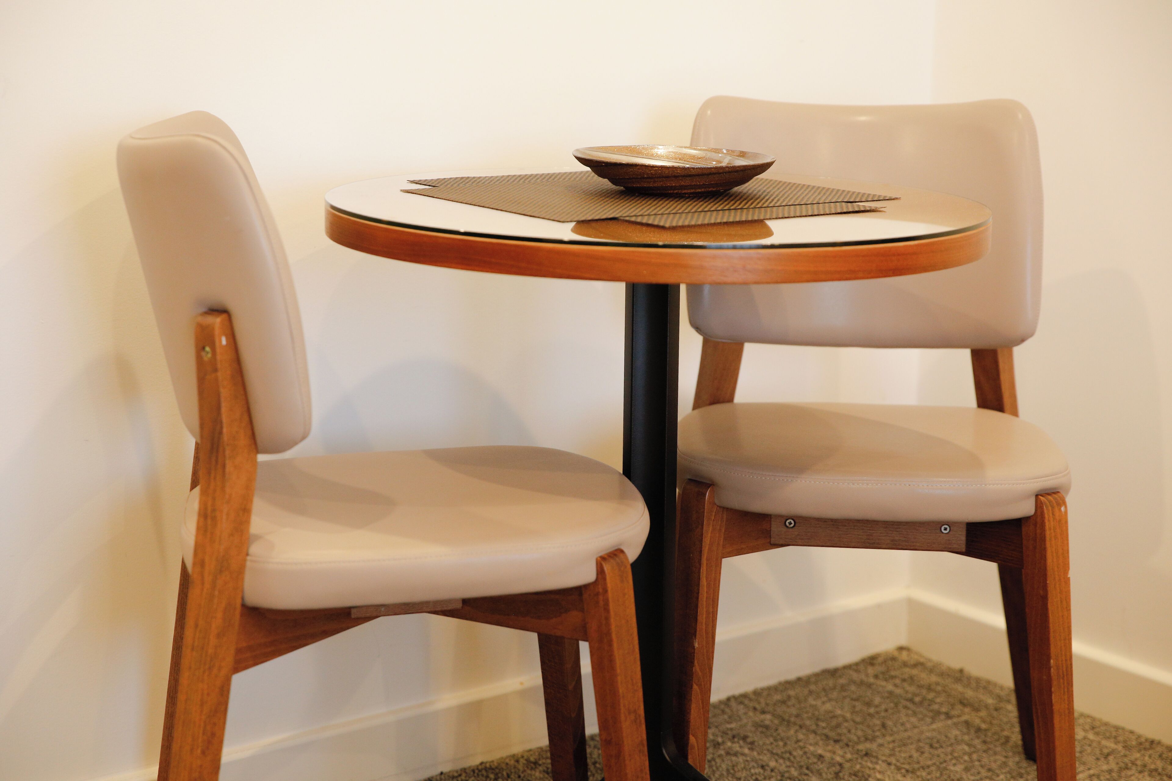 Twee houten stoelen met gewatteerde zittingen en rugleuningen, geplaatst rond een klein rond tafeltje met een schaal erop.