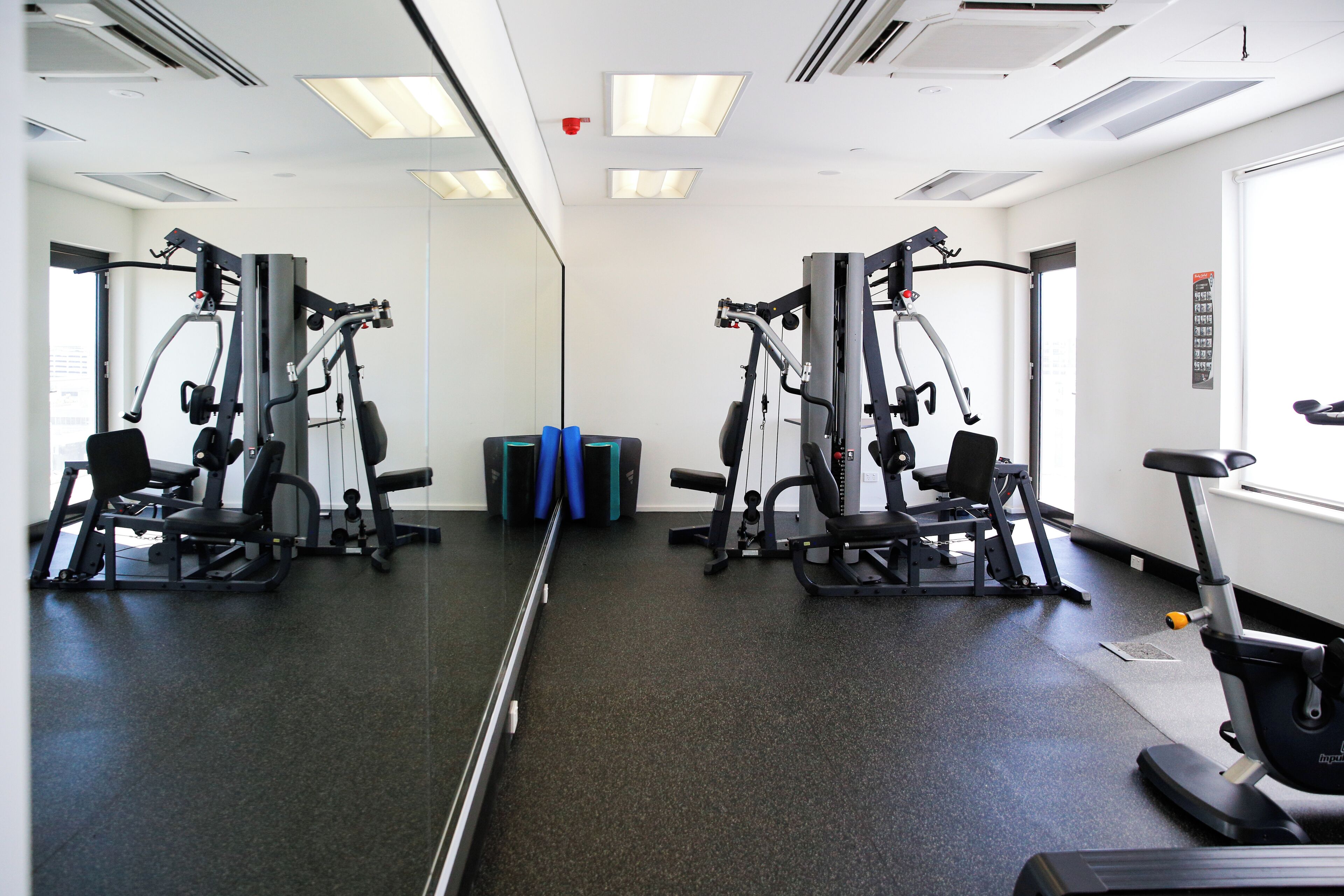 Un gimnasio con paredes de espejo, equipamiento de ejercicio y una cinta de correr.