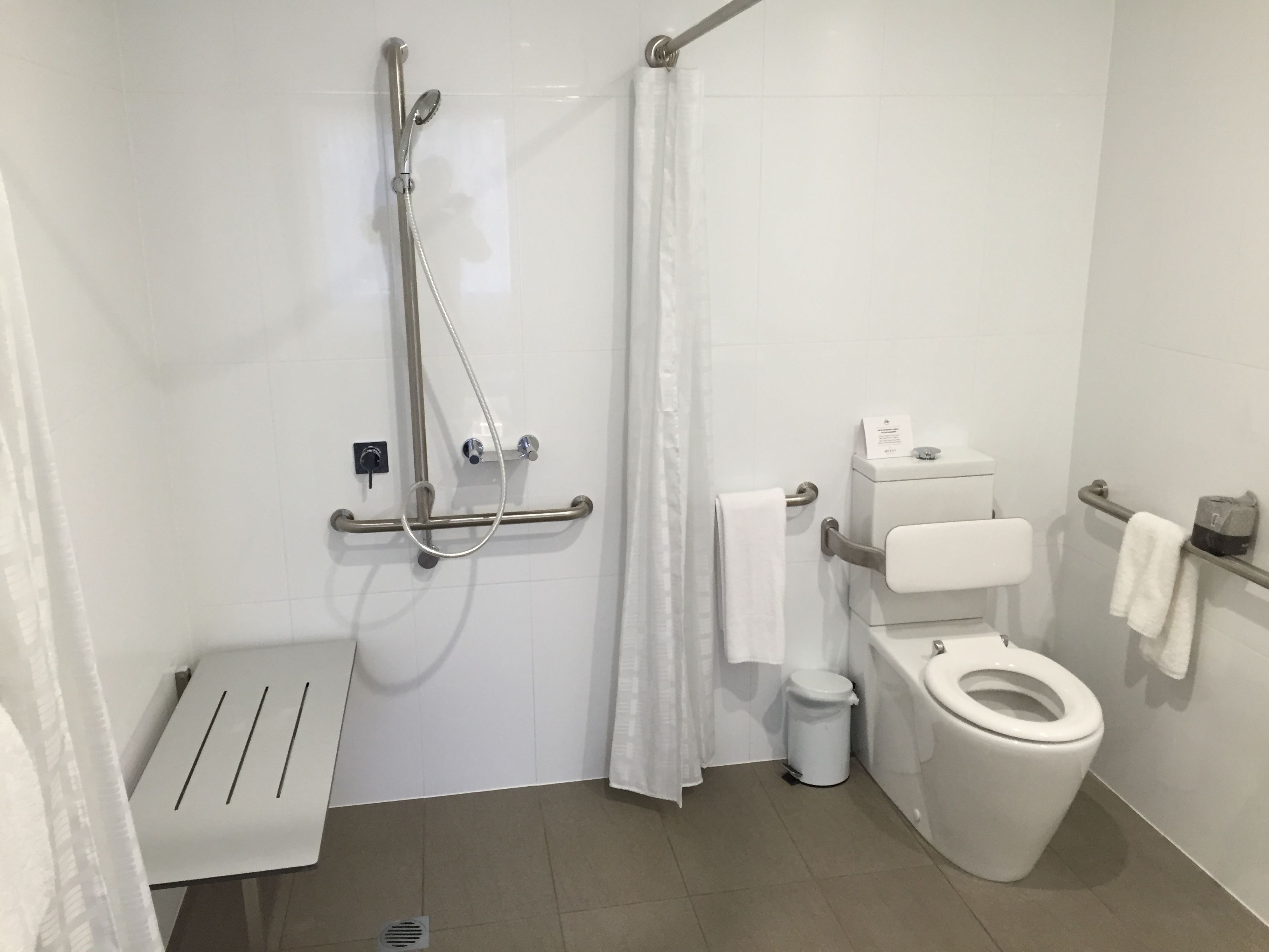 A modern bathroom with a shower, toilet, and a grab bar.