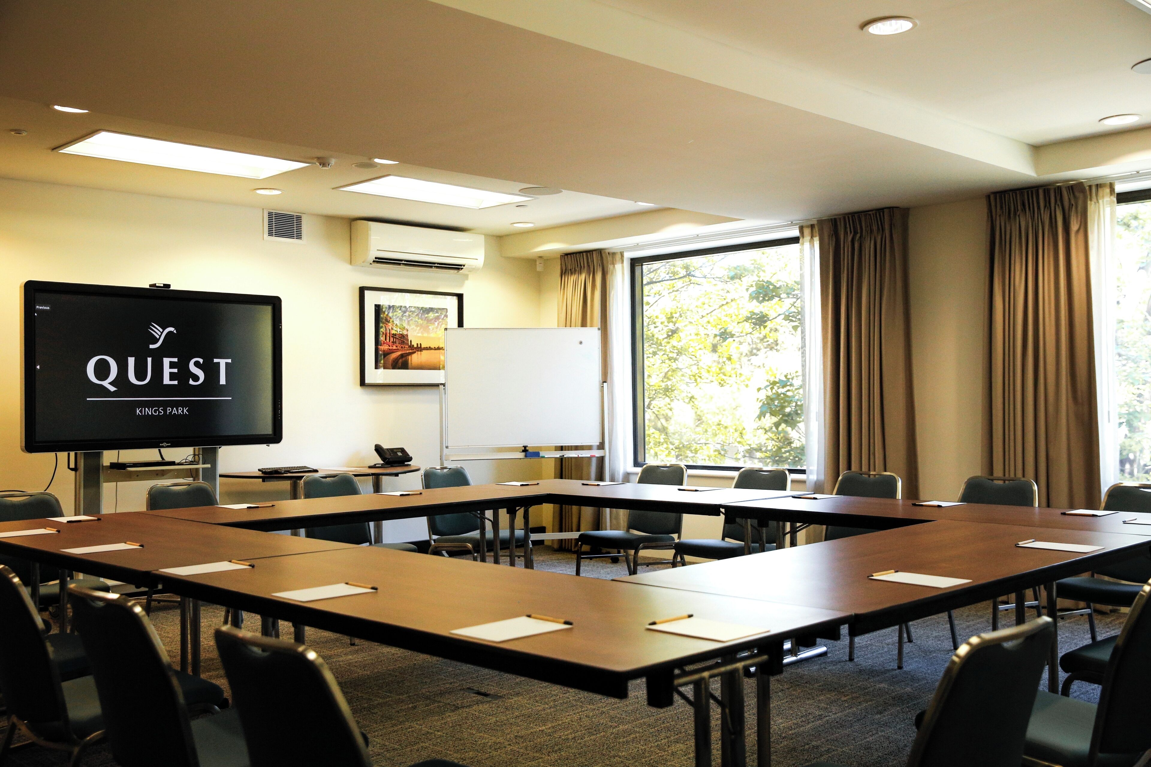 A conference room with a long table, chairs, a projector screen, and a whiteboard.
