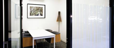 A modern office space with a white table, two black chairs, a framed picture on the wall, and a tall floor lamp.