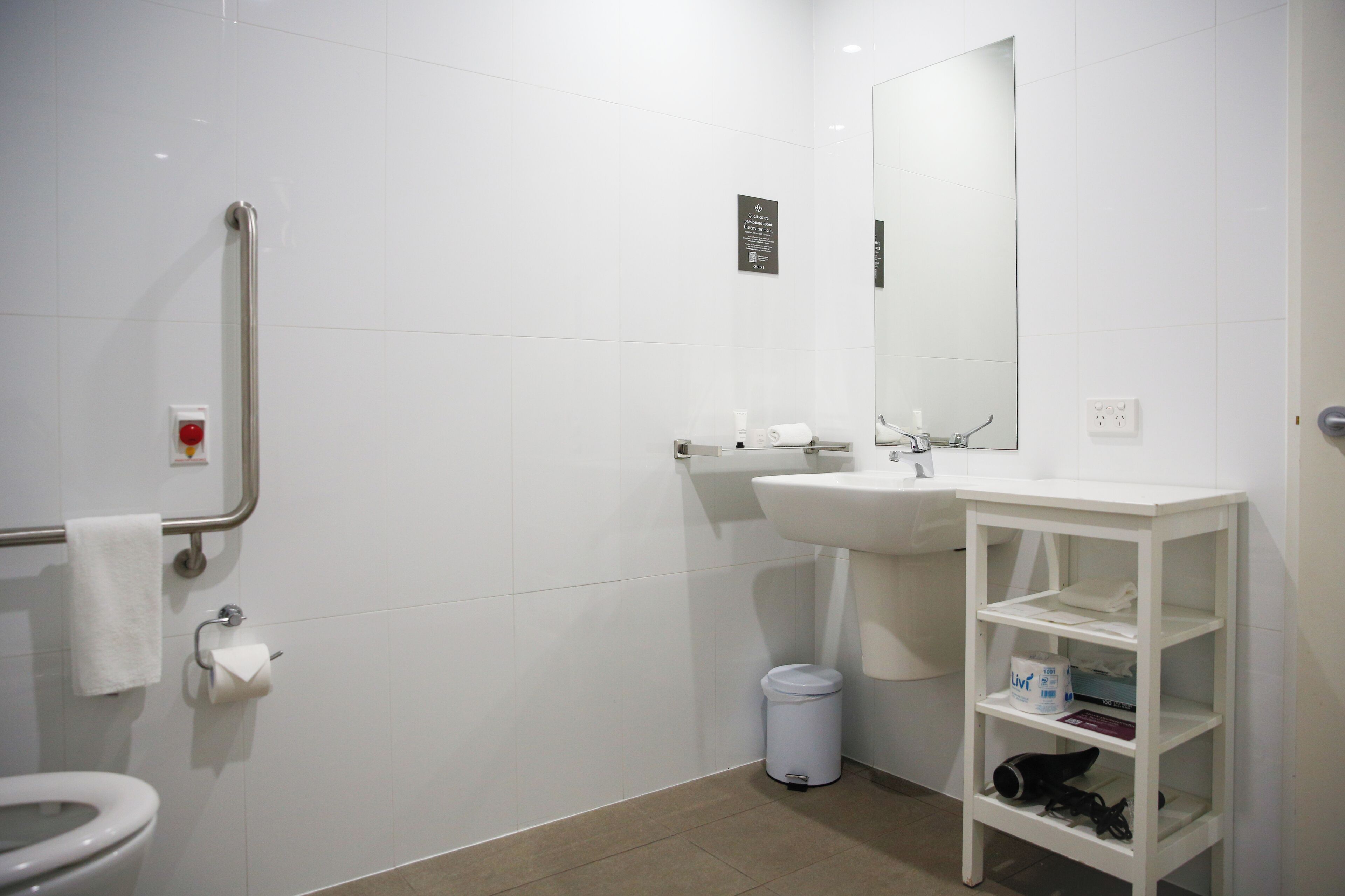 A modern bathroom with a toilet, sink, mirror, and a white shelf unit.