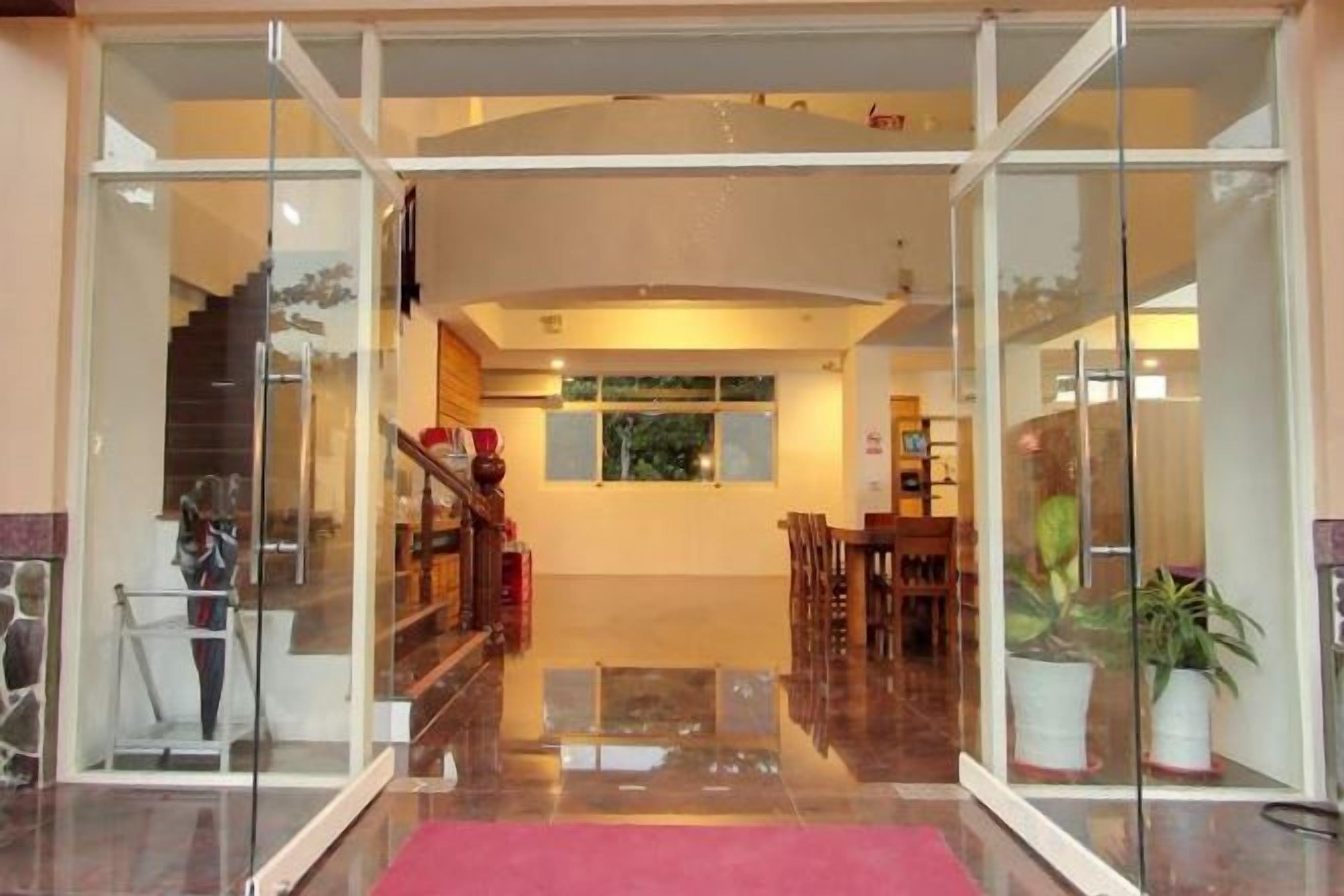 Un vestíbulo de hotel con entrada de vidrio, alfombra roja, una escalera y un mostrador de recepción.