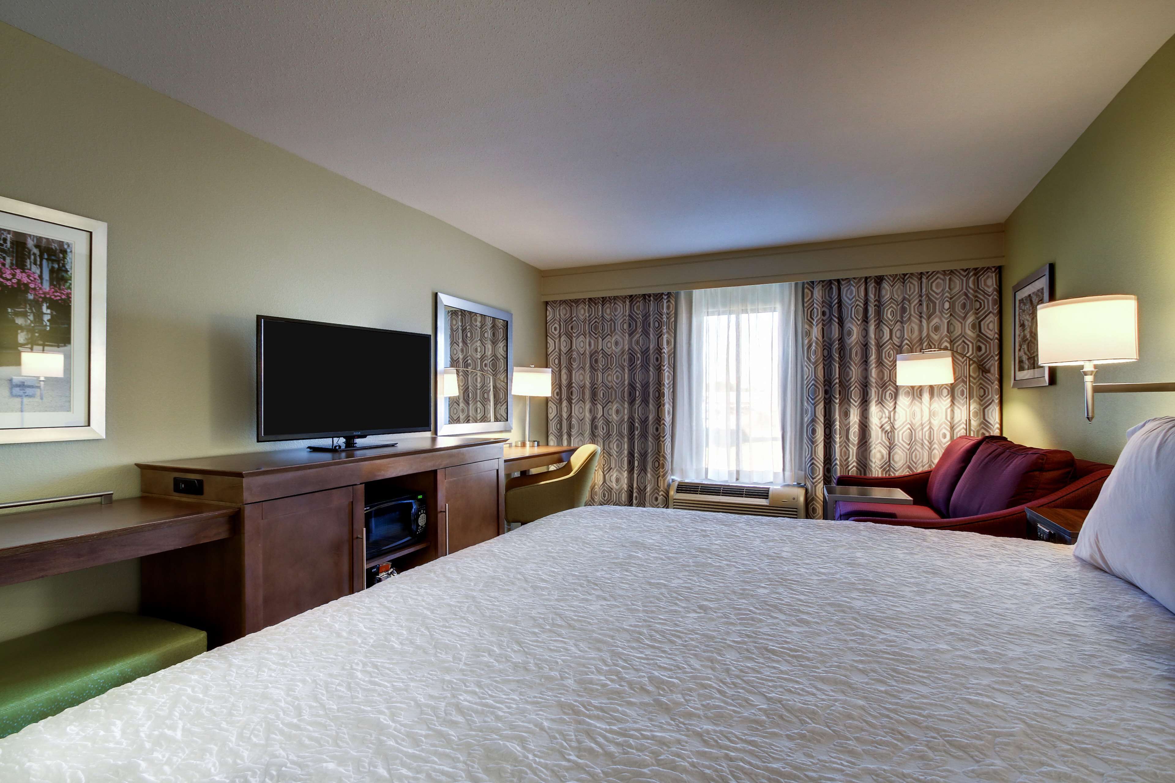 A hotel room with a large bed, a desk with a television, a chair, and a red sofa.
