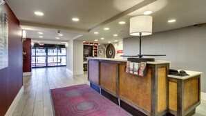Un espace d’accueil avec un comptoir en bois, une moquette rouge et une grande horloge murale.