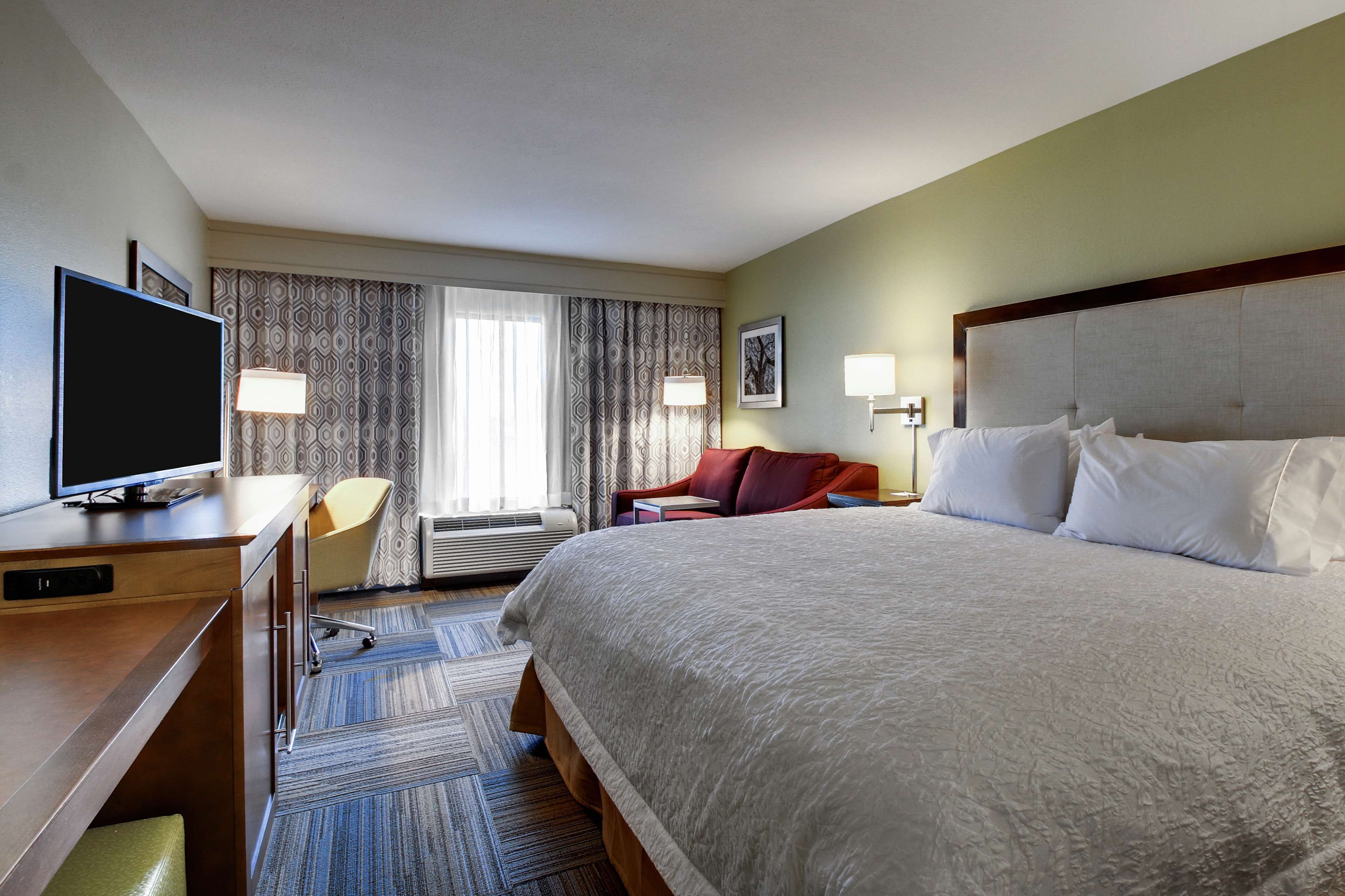 A hotel room with a large bed, a desk with a TV, a chair, and two bedside lamps.