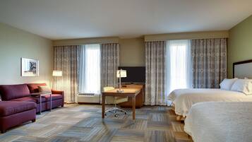 Ein Hotelzimmer mit einem Bett, einem Schreibtisch mit Stuhl, einer Couch und zwei großen Fenstern mit Vorhängen.