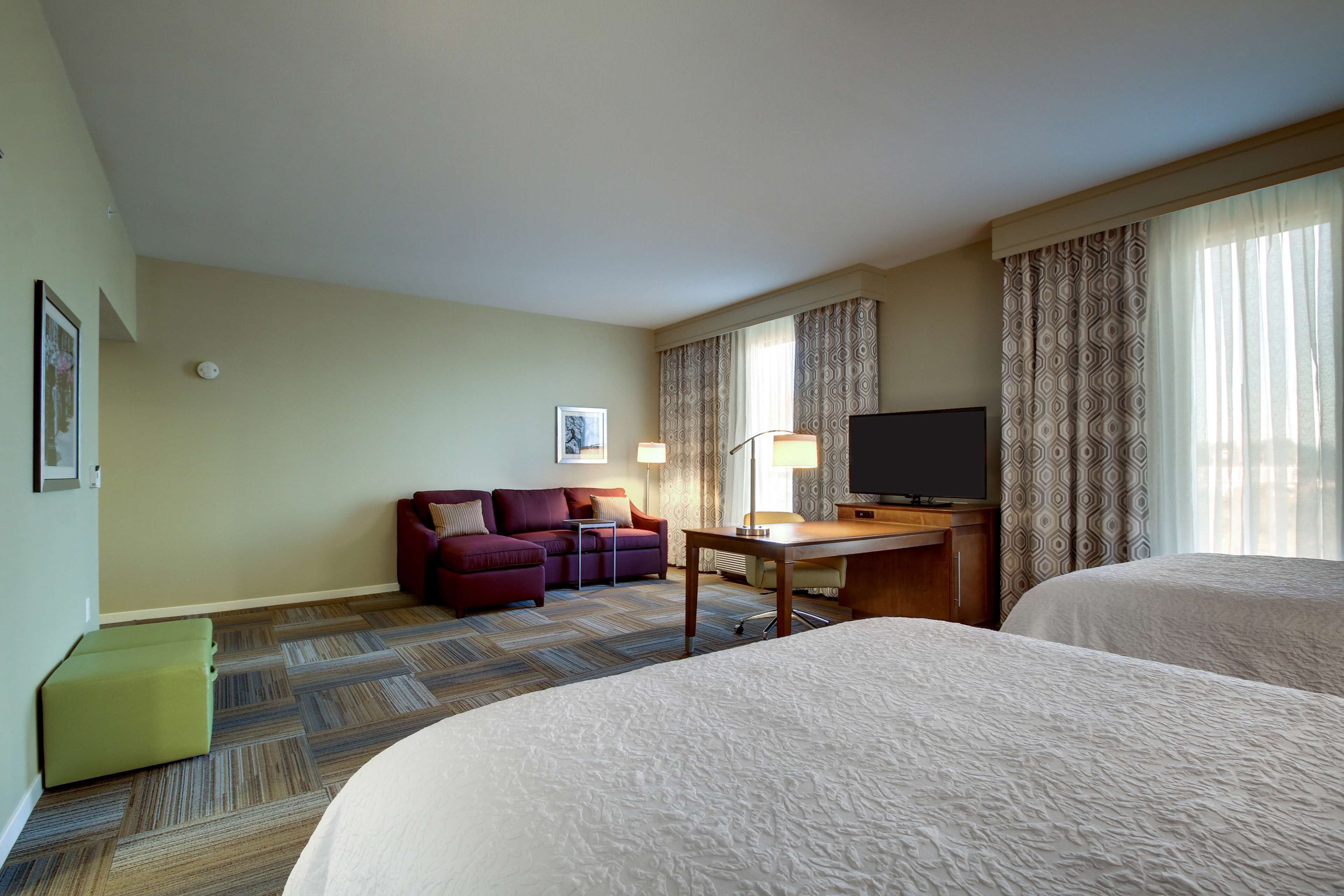 Una habitación de hotel con una cama grande, un escritorio con televisor, un sofá y una cortina estampada.