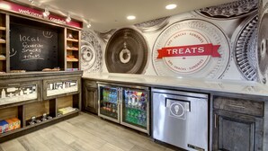 Un bar proposant des collations, avec un menu écrit à la craie, des distributeurs de boissons réfrigérés et une fresque murale faisant la publicité de diverses gourmandises.