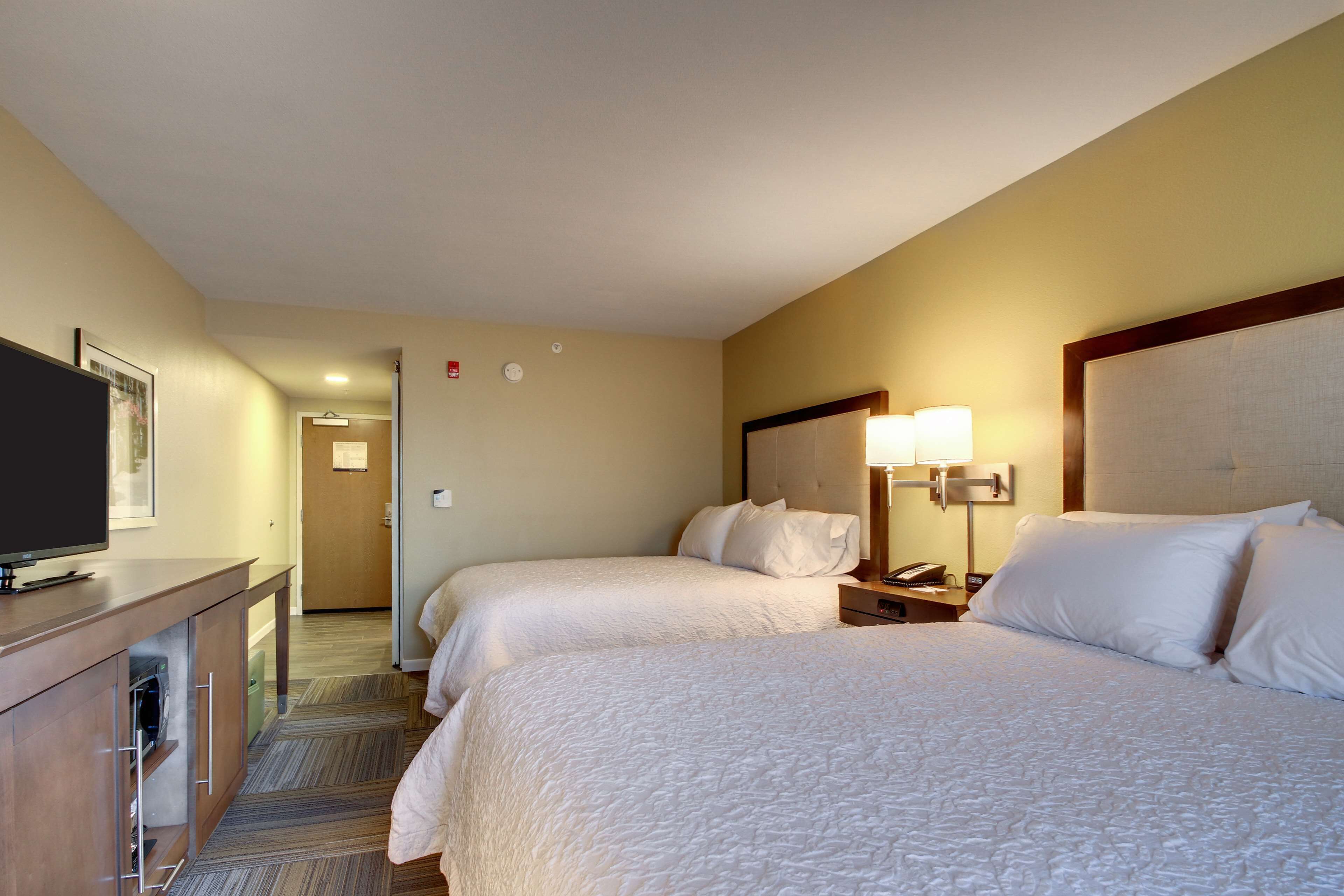 Una habitación de hotel con dos camas, televisión, escritorio y lámpara.