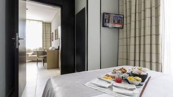 Habitación de hotel con cama, bandeja de desayuno y televisión mostrando un noticiero.