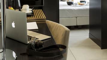 Een moderne hotelkamer met een laptop op een bureau, een camera en een bed, ontbijt zichtbaar op de achtergrond.