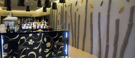 A bar area with a black counter, multiple bottles, and two black bar stools.