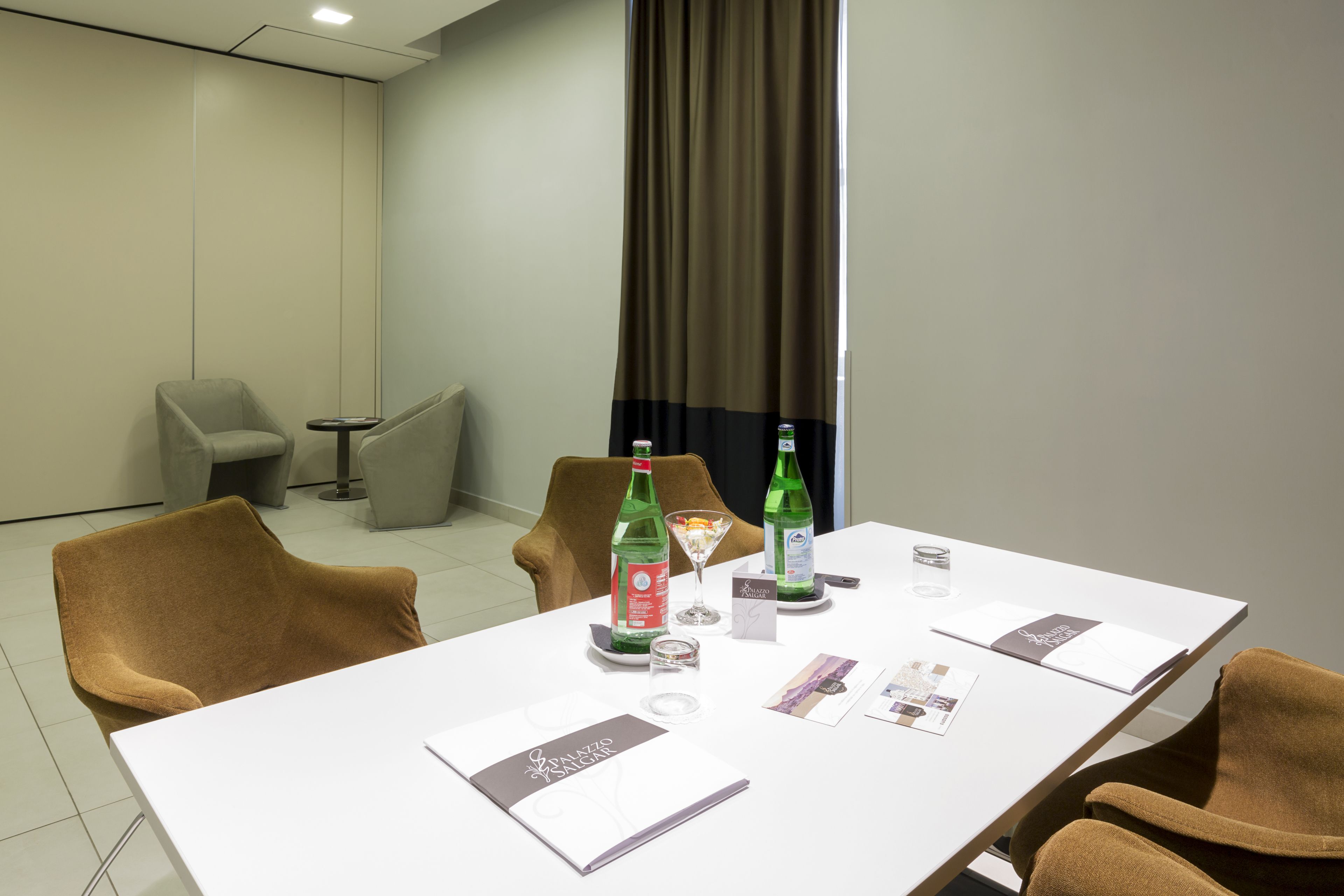 Un salón de conferencias con una mesa blanca, dos sillas, una botella de agua, un vaso y un menú.