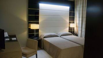 Une chambre d’hôtel comprenant un lit, des tables de chevet, une chaise et un bureau avec une lampe.