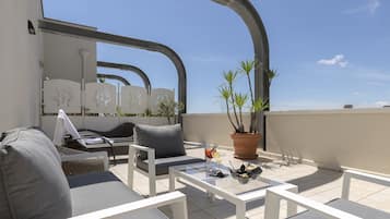 Una terrazza sul tetto con mobili bianchi, un tavolo da pranzo e una pianta in vaso.