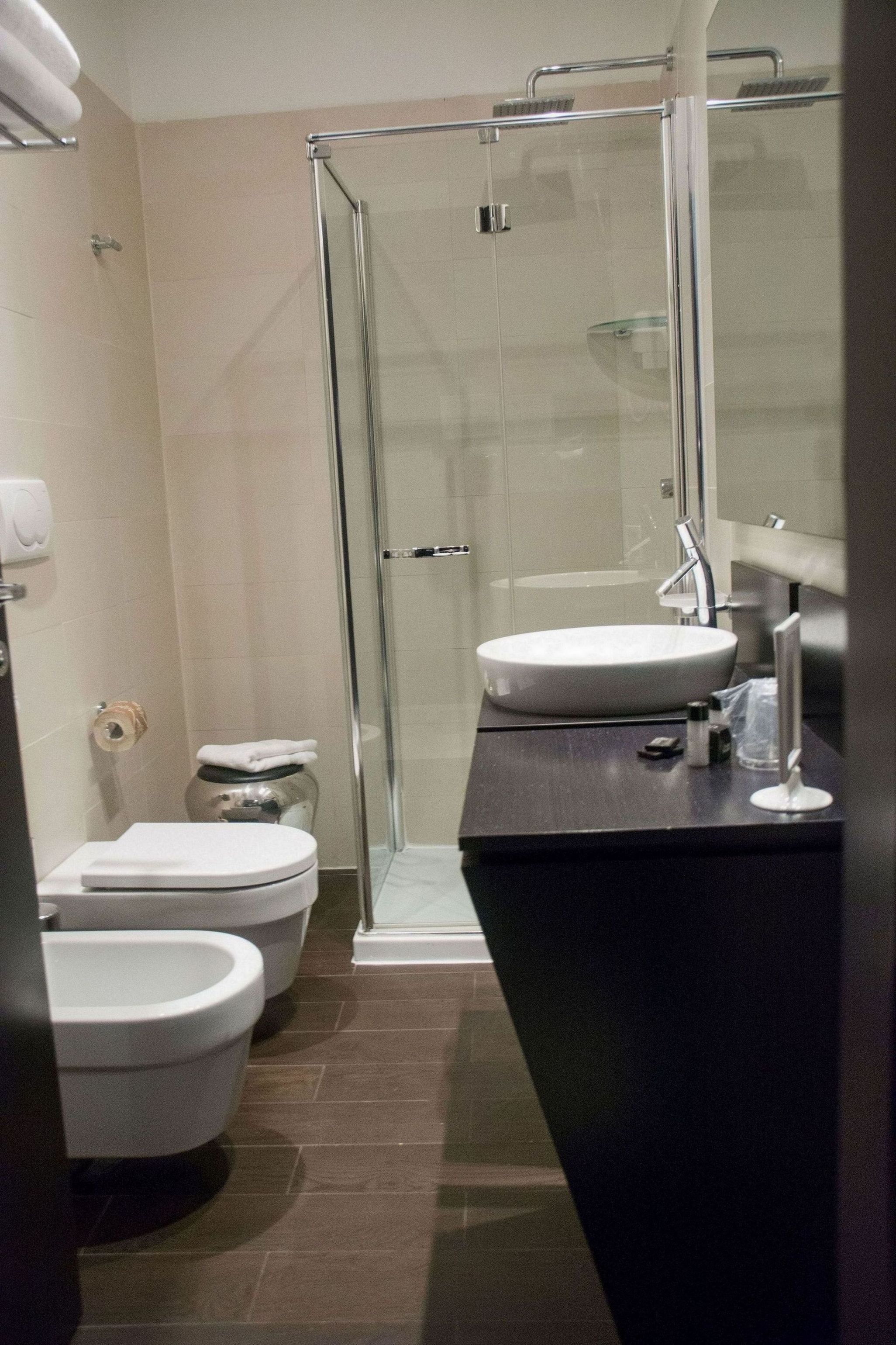 Kylpyhuoneessa on lasiseinällä varustettu suihku, valkoinen pesuallas ja kaksi wc-istuinta.