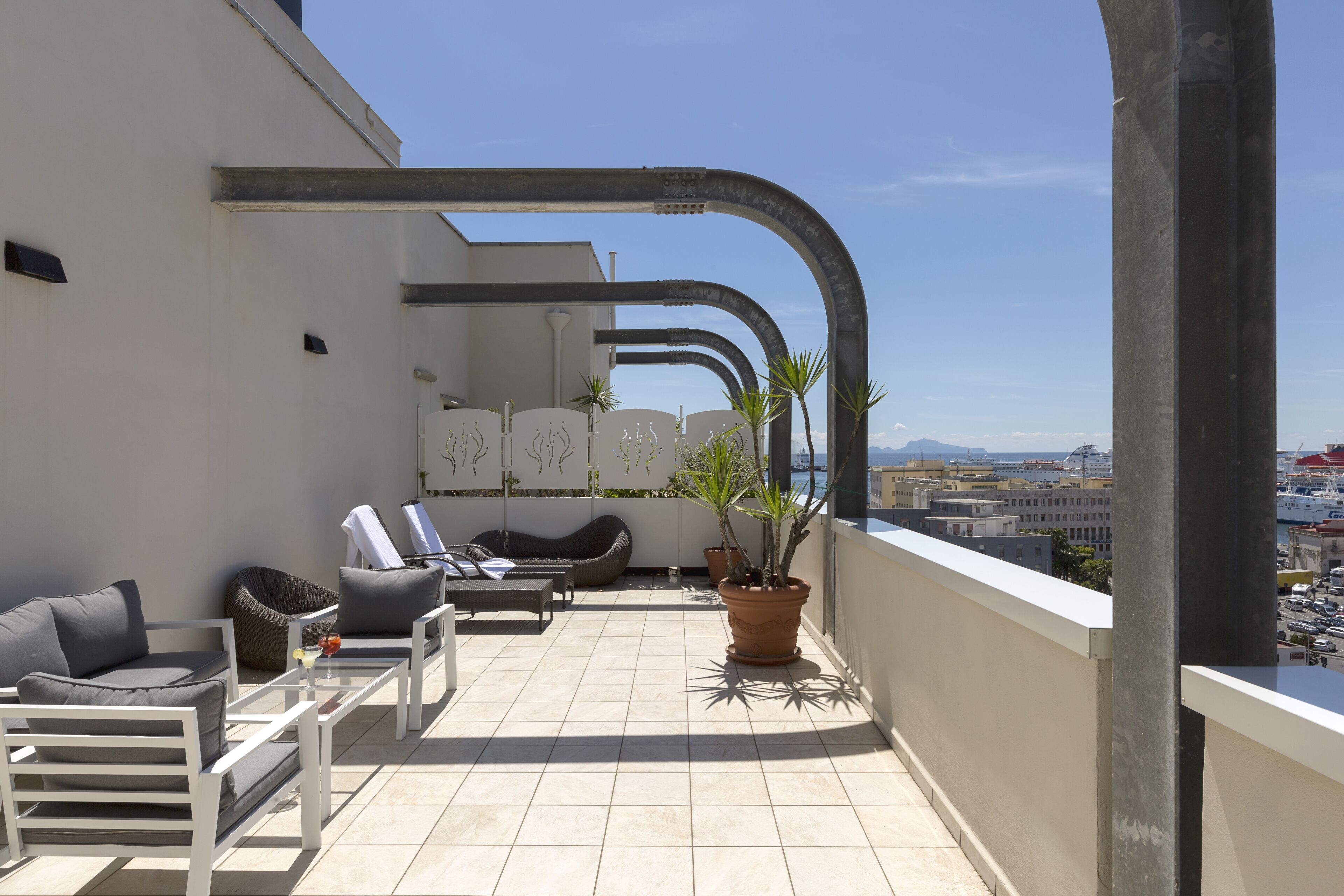 A rooftop terrace with a seating area, potted plants, and a view of the cityscape.