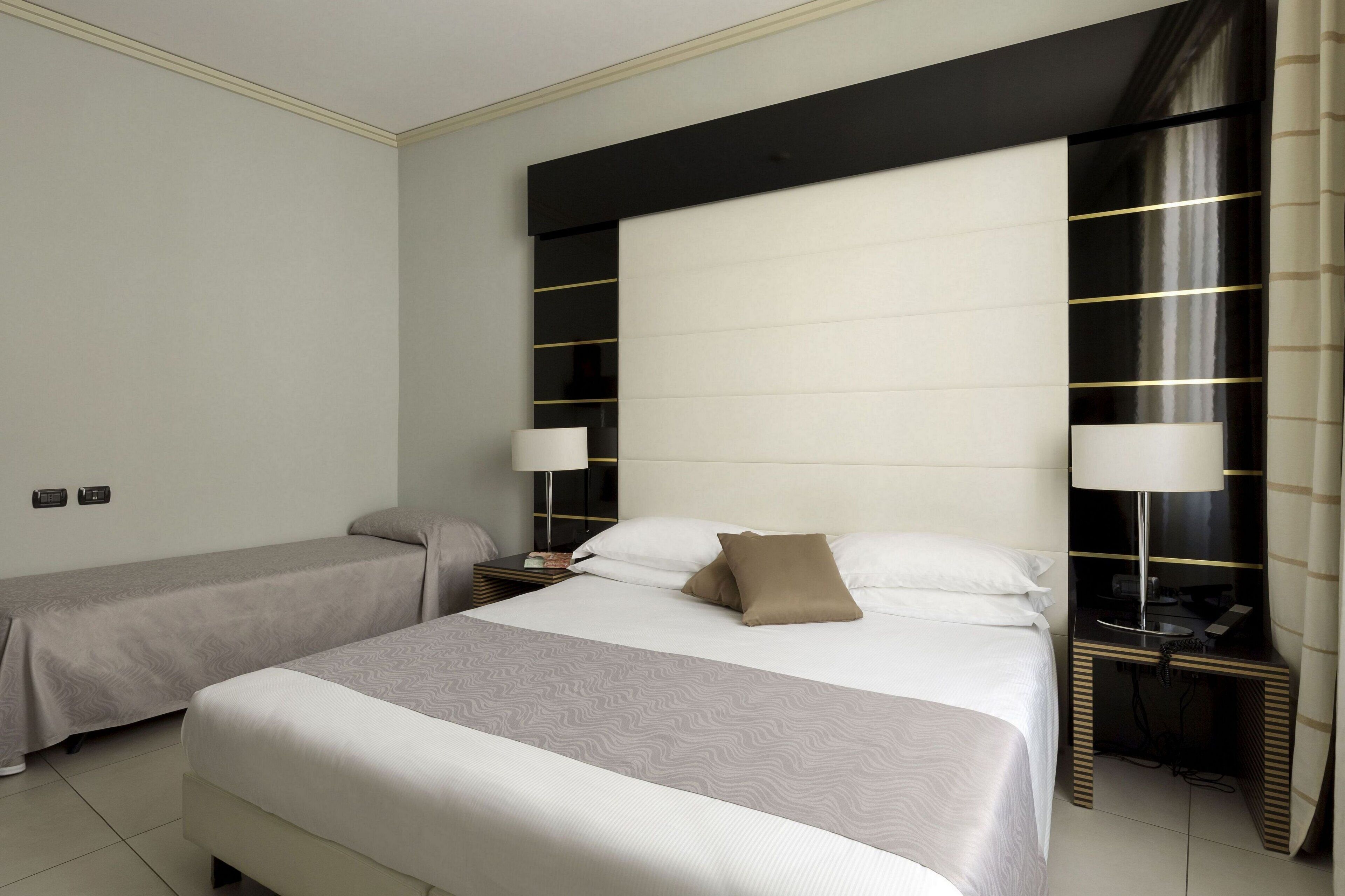 Ett hotellrum med två sängar, en stor sänggavel, sänglampor och ett litet bord.