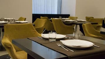 A hotel dining area with tables set for two, featuring yellow chairs and dark table surfaces.