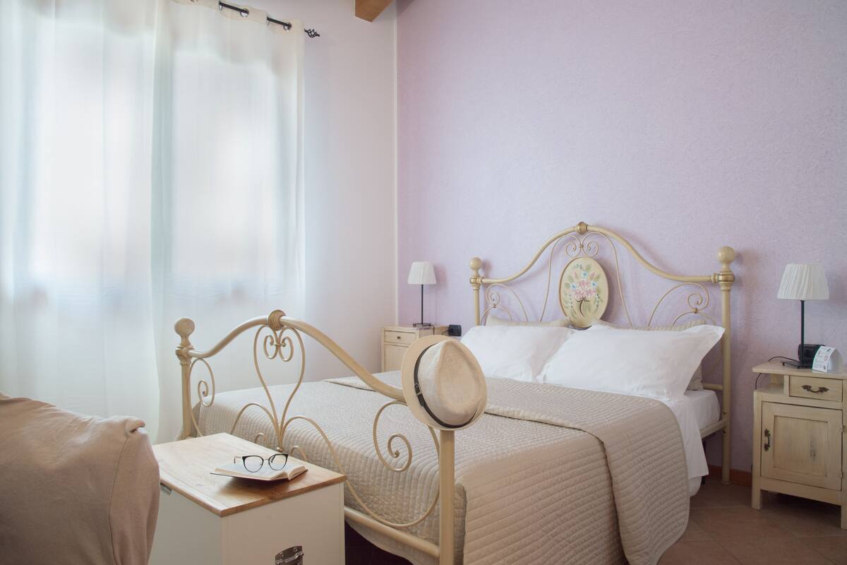 Quarto bem organizado com cama, mesas de cabeceira e apoio para objetos pessoais.
