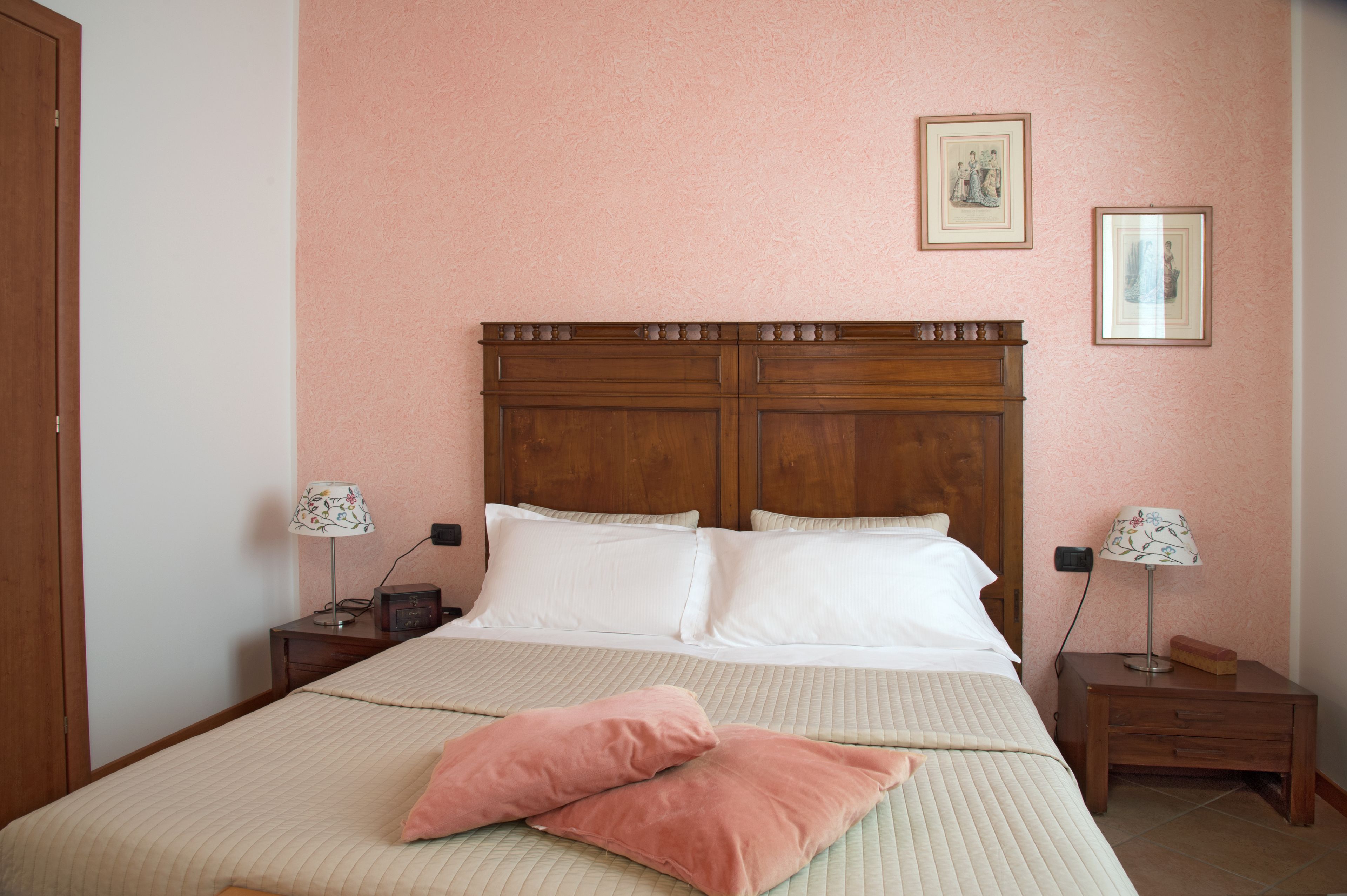 A neatly made bed with a wooden headboard, two bedside tables with lamps, and two framed pictures on the wall.