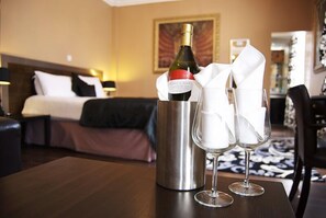 A hotel room with a bed, a bedside table with a wine bottle and glasses, and a nightstand with a lamp. - Villaggio Hotel & Restaurant (Warrington)