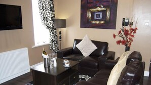 A modern living room with a dark brown leather sofa, a coffee table, and a patterned rug. - Villaggio Hotel & Restaurant (Warrington)