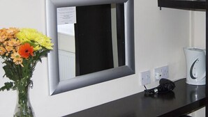 A room with a flat-screen TV mounted above a mirror, a vase with flowers on a table, and a kettle on a shelf. - Villaggio Hotel & Restaurant (Warrington)