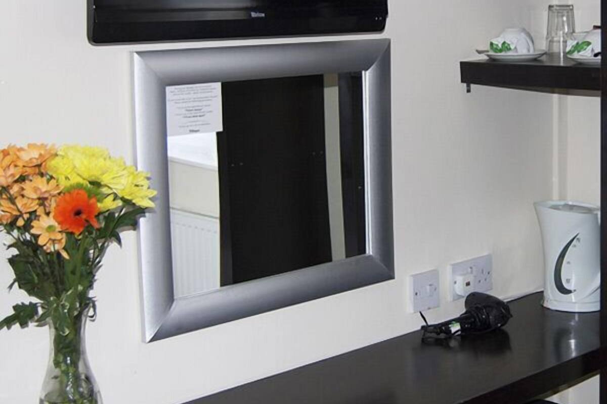 A room with a flat-screen TV mounted above a mirror, a vase with flowers on a table, and a kettle on a shelf.