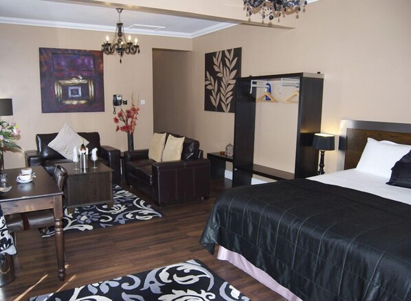 Une chambre d’hôtel avec un grand lit, un bureau avec une chaise, un canapé, un lustre et un tableau au mur.