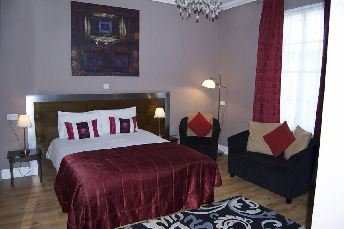 A hotel room with a large bed, a sofa, a floor lamp, and a painting on the wall.