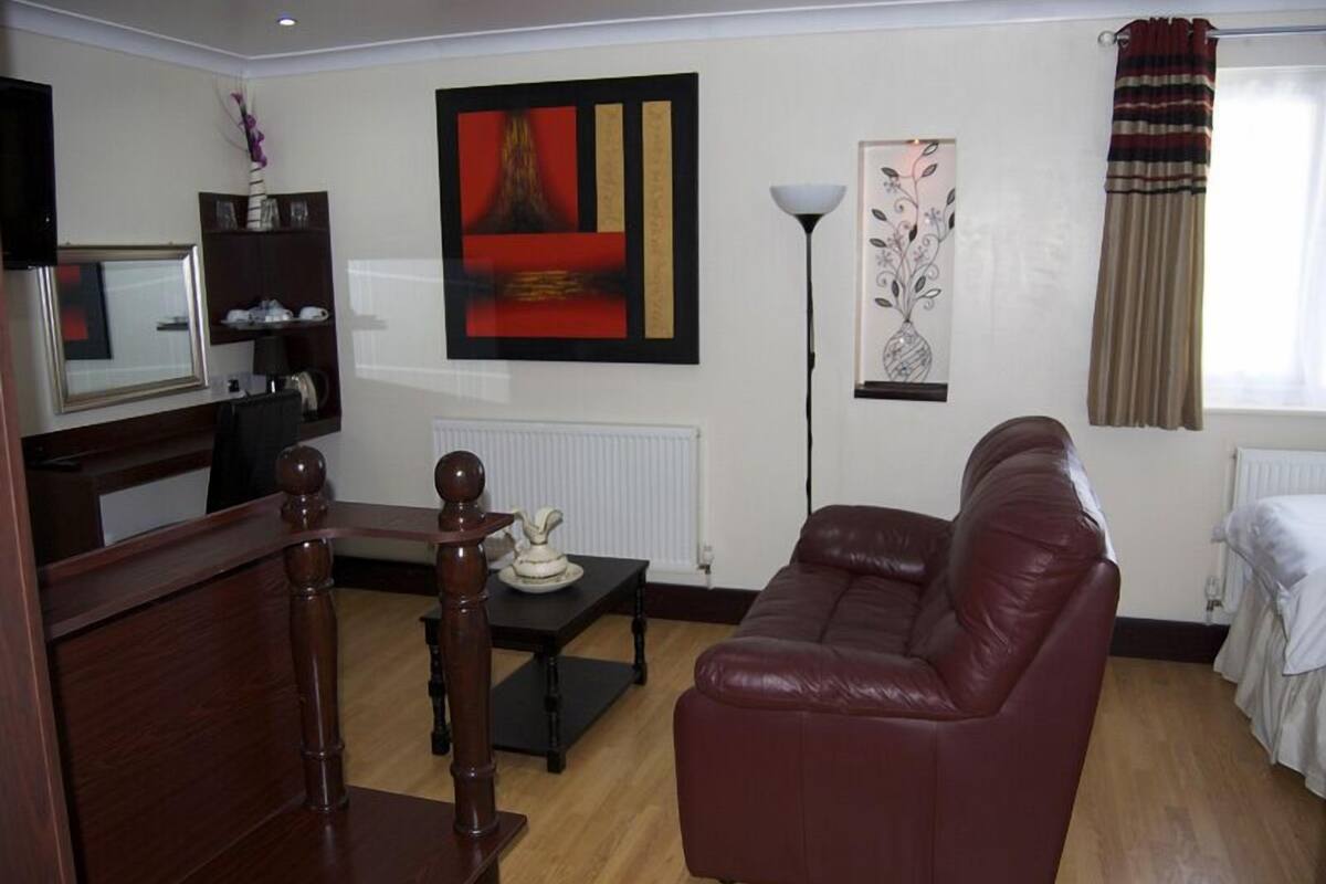 A living room with a dark brown leather sofa, a wooden coffee table, a TV on a stand, and a painting on the wall.