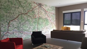 A modern living room with a large map on the wall, a red chair, a black armchair, a beige sofa, and a wooden coffee table with magazines. - Dans Les Vignes (Chamery)