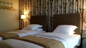 A hotel room with two beds, a nightstand, a lamp, and a wall with vertical patterned wallpaper. - Dans Les Vignes (Chamery)