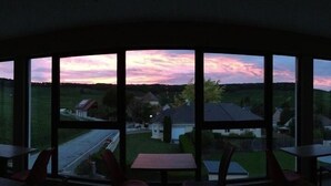 A room with large windows offering a view of a rural landscape during sunset. - Dans Les Vignes (Chamery)