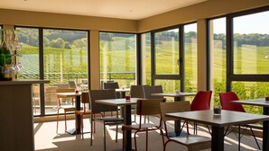 A modern dining area with large windows offering a view of a vineyard. Tables and chairs are arranged for dining. - Dans Les Vignes (Chamery)