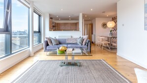A modern living room with a glass coffee table, a sofa, and a view of the city through large windows.