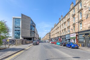 A street with parked cars, a modern building, and traditional buildings with shops. - Executive 7 Apartments (Glasgow)