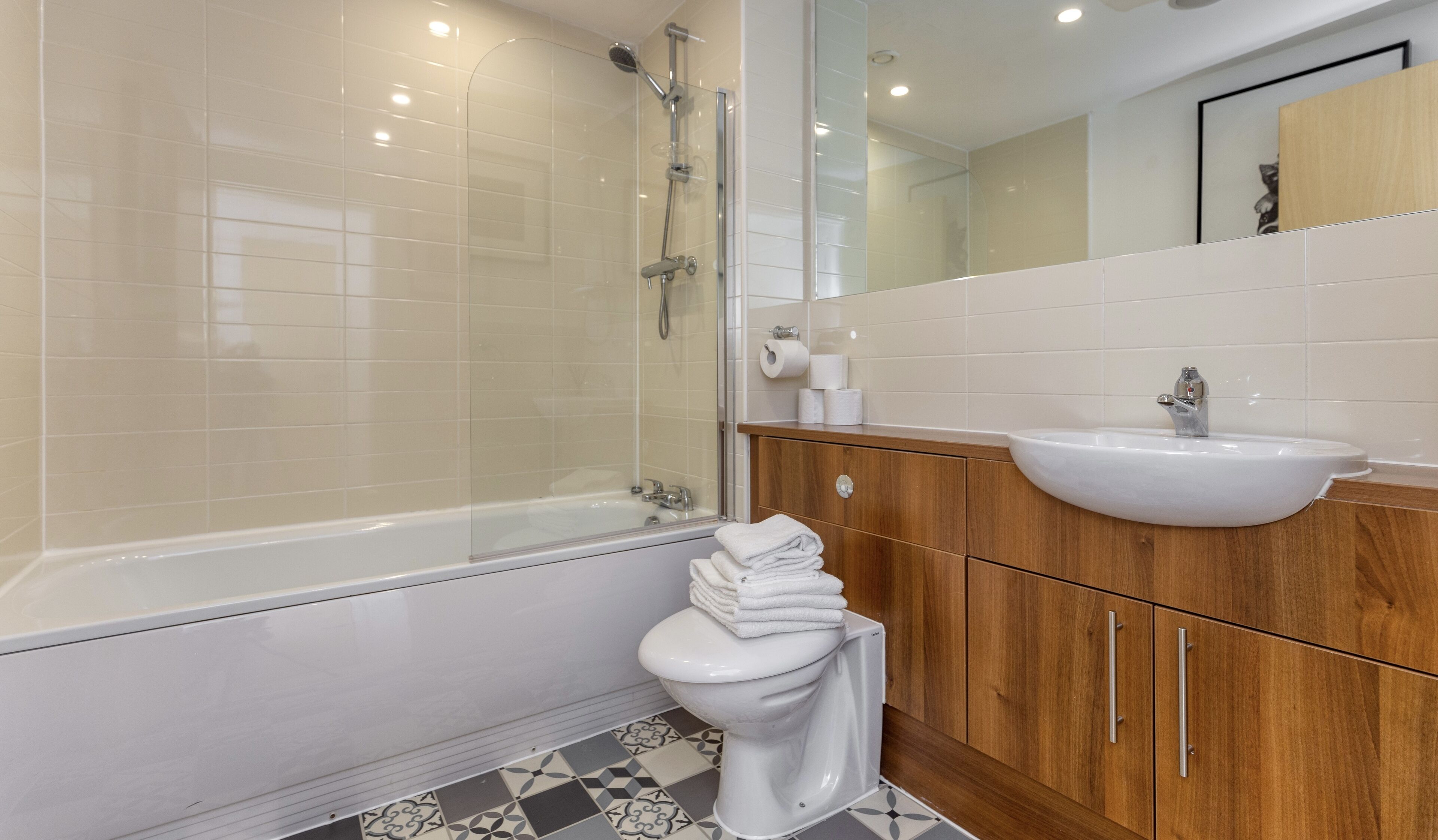 A modern bathroom with a glass-enclosed shower, a white toilet, and a wooden vanity with a sink.