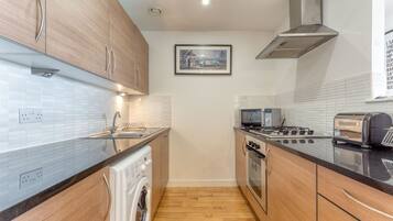 A modern kitchen with wooden cabinets, a stainless steel range, a built-in oven, a microwave, and a washing machine.