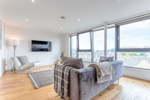 A modern living room with a grey sofa, a floor lamp, and a large window offering a city view. - Executive 7 Apartments (Glasgow)