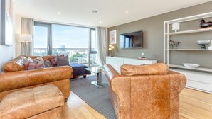 A modern living room with leather sofas, a glass coffee table, and a flat-screen TV mounted on the wall.