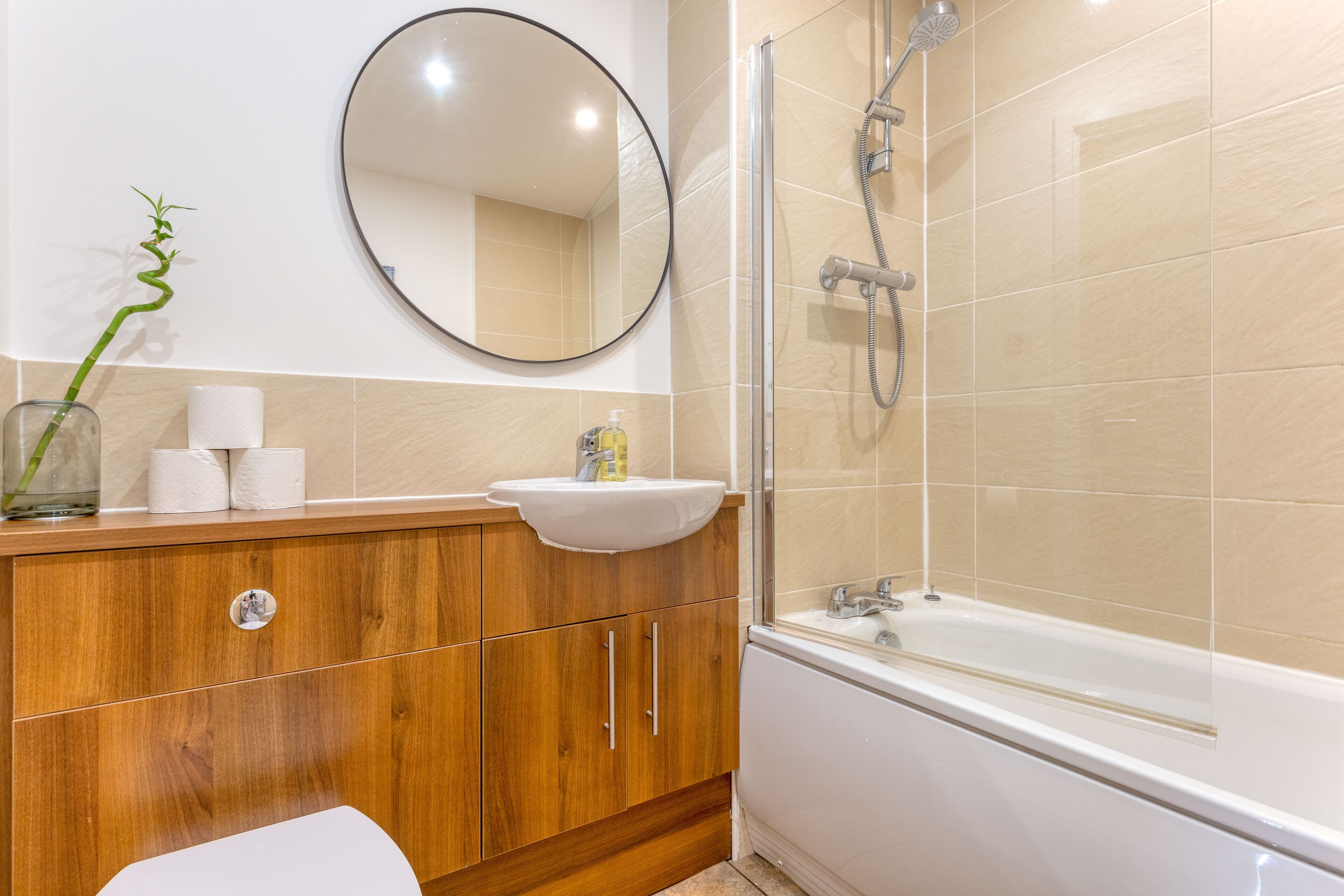 A bathroom with a wooden vanity, a sink, a mirror, and a shower.