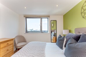 A bedroom with a bed, a chair, a dresser, and a window with a view. - Executive 7 Apartments (Glasgow)
